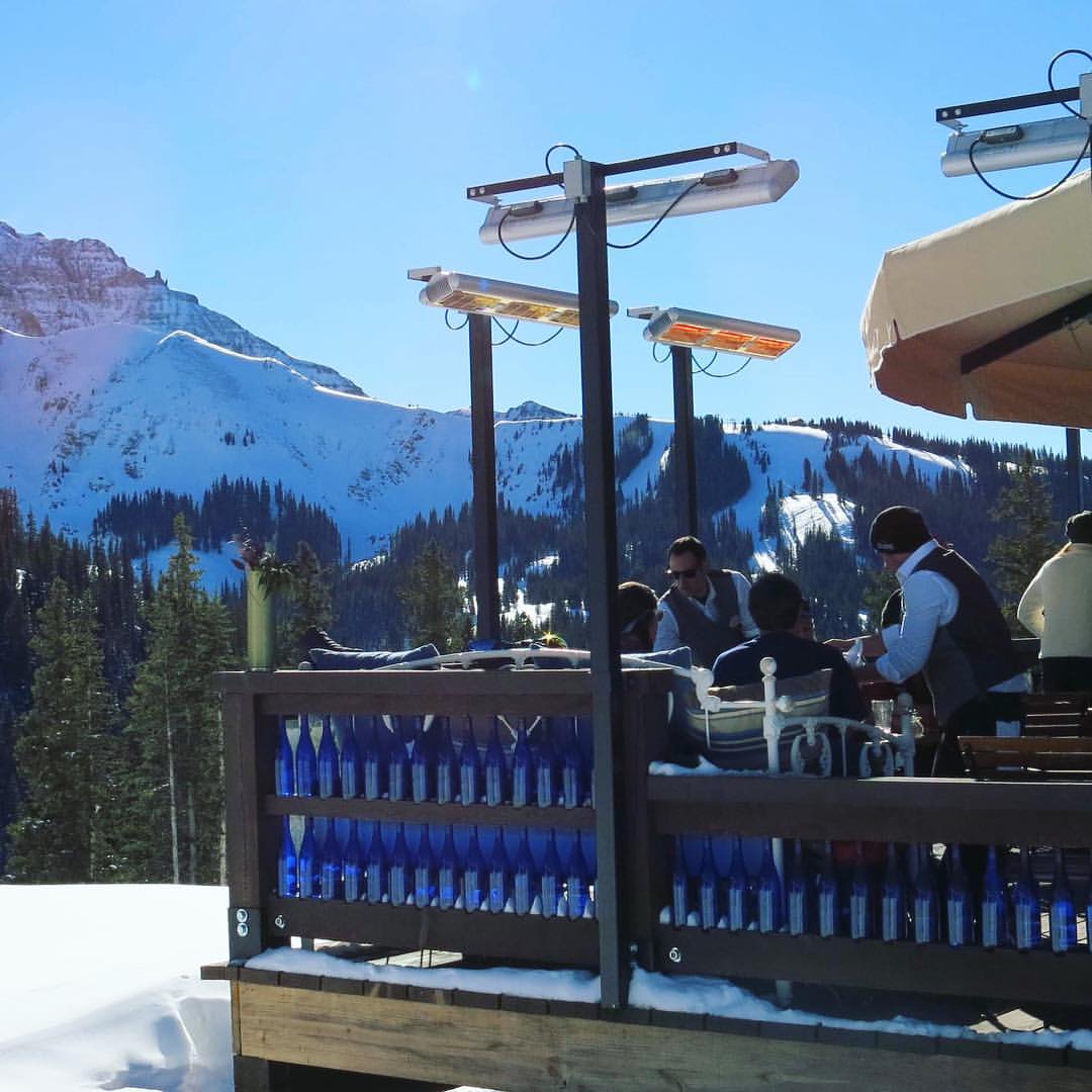 Infrazářič Tansun Monaco Single 1,5 kW v instalaci na restaurační terase – ukázka prémiového Low Glare quartzového zářiče s minimální svítivostí a zlatým reflektorem ve večerní atmosféře s tlumeným osvětlením, kde zářič nenarušuje estetiku prostoru