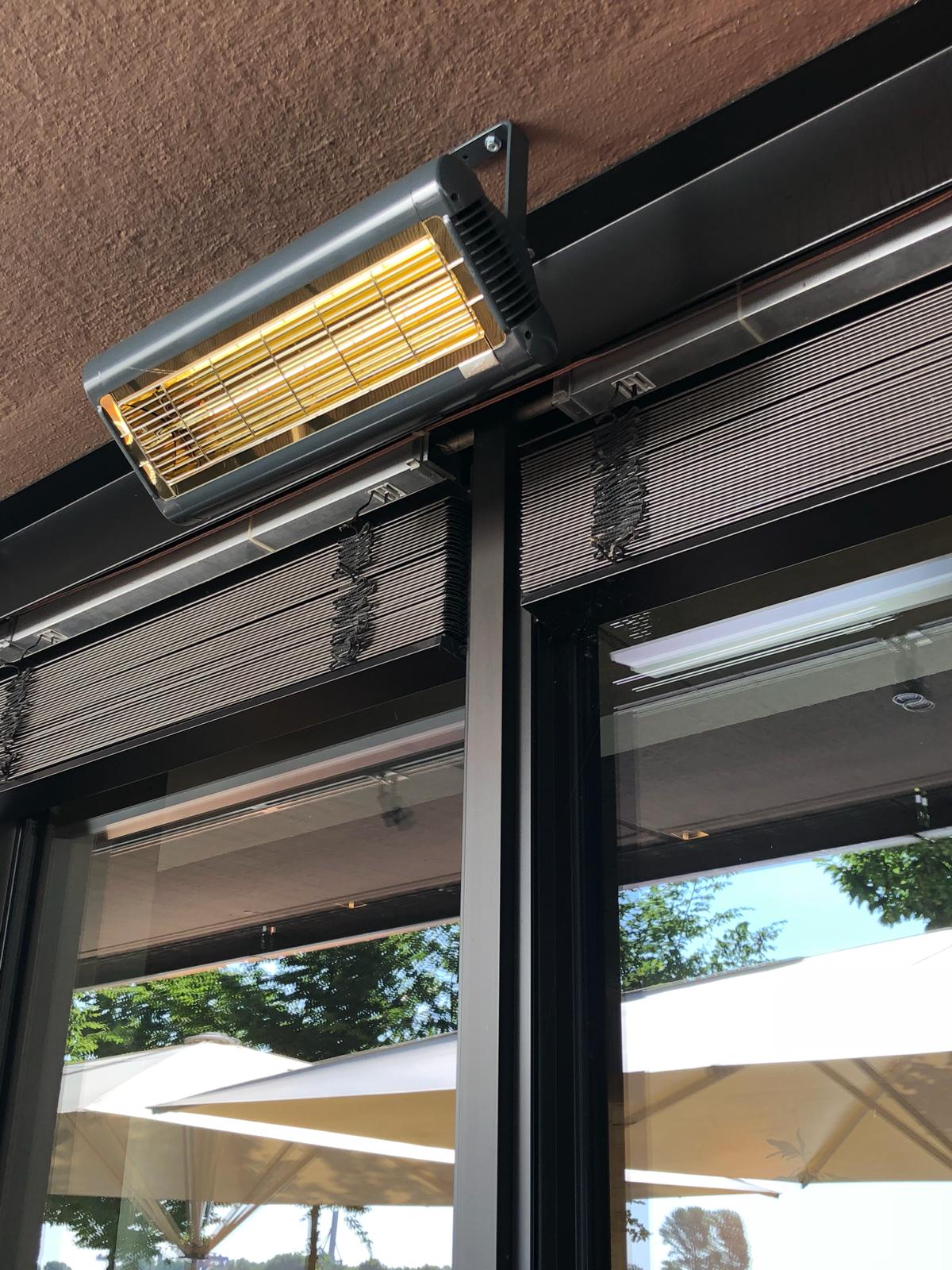 Infrazářič Tansun Monaco Single 1,5 kW v instalaci na restaurační terase – ukázka prémiového Low Glare quartzového zářiče s minimální svítivostí a zlatým reflektorem ve večerní atmosféře s tlumeným osvětlením, kde zářič nenarušuje estetiku prostoru